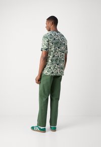 Short-sleeve green floral-patterned shirt, light beige flowers, paired with green trousers and green sneakers with white stripes.