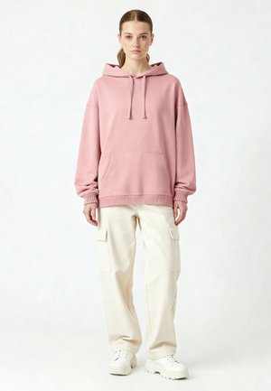 Felpa rosa oversize con cappuccio e lacci, tasca frontale e polsini a coste, abbinata a pantaloni cargo crema e sneakers bianche chunky.