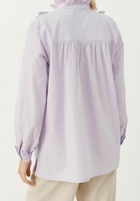 Camicia a maniche lunghe di un leggero viola, con schiena plissettata, dettagli in pizzo sul colletto e polsini con bottoni. Presenta abbottine laterali all'orlo.
