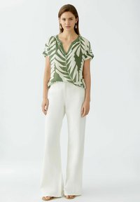 Groene bloemetjesblouse met een v-hals en korte mouwen, gecombineerd met witte wijde broek en beige sandalen. Soepele stoftextuur.