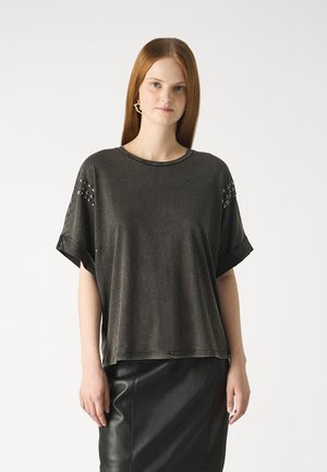 T-shirt oversize gris foncé en tissu doux, avec des manches courtes retroussées et des accents cloutés sur les épaules. Porté avec une jupe en cuir noire.