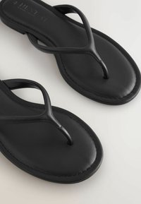 Par sort sorte læder flip-flop sandaler med minimal syning på hvid baggrund, viser nærbillede af stropper og fodseng.