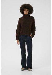Barna kötött pulóver magas gallérral, sötét denim, bővülő farmernadrággal párosítva. Csíkos lapos cipők teszik teljessé az öltözetet. Sima textúra, laza fazon.