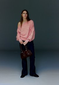 Pink strikket sweater med et design, der afslører skuldrene, brede ærmer og tekstureret mønster, kombineret med mørke, vide jeans og en brun håndtaske.