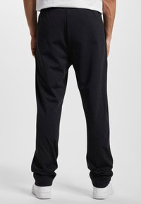 Black cotton joggers with a relaxed fit, featuring an elastic waistband and tapered cuffs, paired with white sneakers.