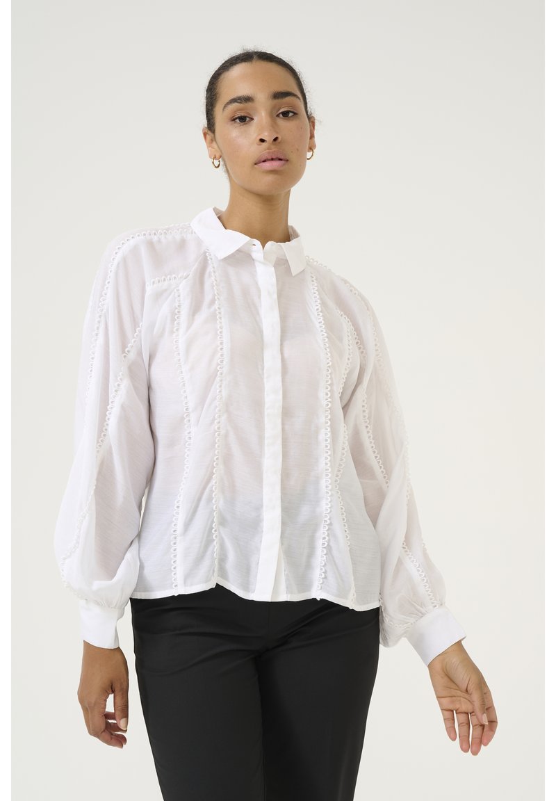 Weißes Button-Down-Hemd aus einem transparenten, leichten Stoff. Verziert mit dekorativen Besätzen entlang der Nähte und voluminösen, gerafften Ärmeln.