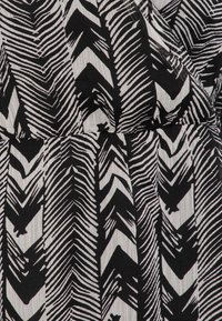 Tessuto in bianco e nero con un motivo di linee zigzag diagonali e forme di foglie astratte su uno sfondo texturizzato.