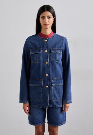 Denimjack met gouden knopen, twee borstzakken en een contrasterende rode kraag. Gecombineerd met denimshorts, beide in een middelmatige wassing.
