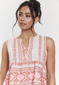 Leichtes, ärmelloses Tunika mit V-Ausschnitt, die komplizierte geometrische Muster in Pink und Weiß zeigt und einen lässigen Sitz für Komfort bietet.