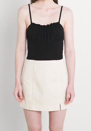 Schwarzes ärmelloses Crop-Top mit geraffter Textur, kombiniert mit einem beige hohen Minirock, der über eine Schlitze vorne verfügt.