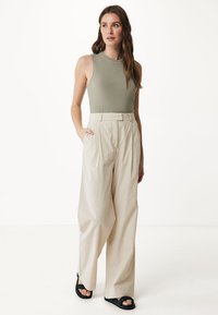 Débardeur en olive clair côtelé associé à un pantalon large taille haute beige, doté de poches latérales et de sandales noires à brides.