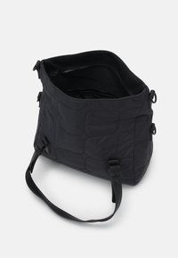 Schwarze gesteppte Tasche mit einer weichen Textur, ausgestattet mit einem einzelnen verstellbaren Schultergurt und einem Reißverschluss-Innenfach. Entwickelt für einfachen Zugang.