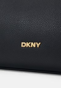 Black leather handbag featuring a textured surface, with a prominent gold "DKNY" logo as an accent.