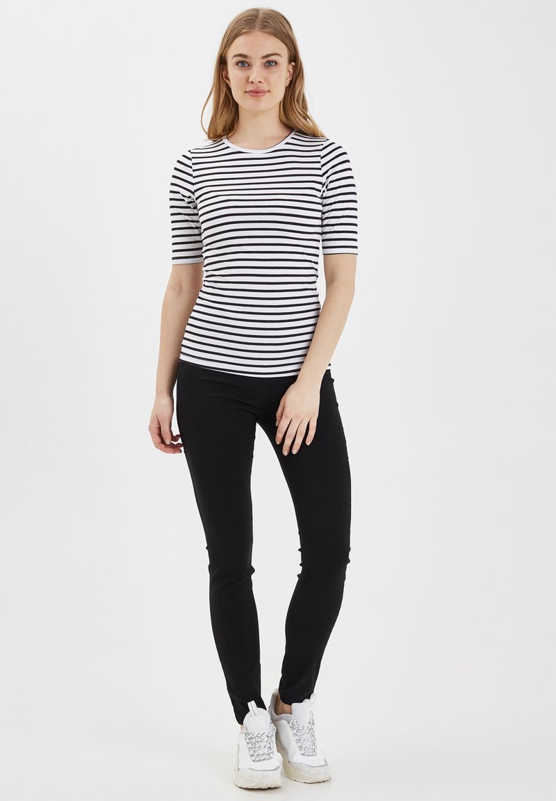 Černobílý pruhovaný top s krátkým rukávem, který je doplněn černými skinny kalhotami a bílými teniskami. Top má kulatý výstřih a slim fit střih.