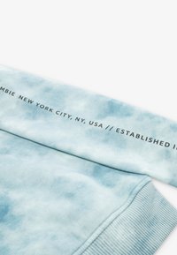Sudadera azul claro con un patrón de tie-dye. Presenta puños acanalados y un logotipo impreso que detalla "Abercrombie Nueva York, NY, EE.UU."