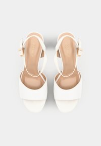 Tacones slingback blancos con un acabado suave, puntera abierta y una hebilla con acentos dorados. Plataforma plana y correas delgadas. Plantilla suave y en tonos neutros.