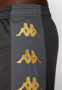 Hallid hallid sportlikud lühikesed püksid, millel on külgedel kolm kuldset logo, sujuva tekstuuri ja elastse vöökoha.