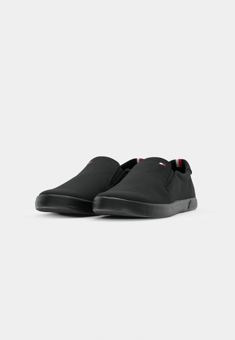 Chaussures noires à enfiler avec une tige en toile lisse, semelles en caoutchouc et accents rouge et blanc contrastants sur la doublure intérieure.