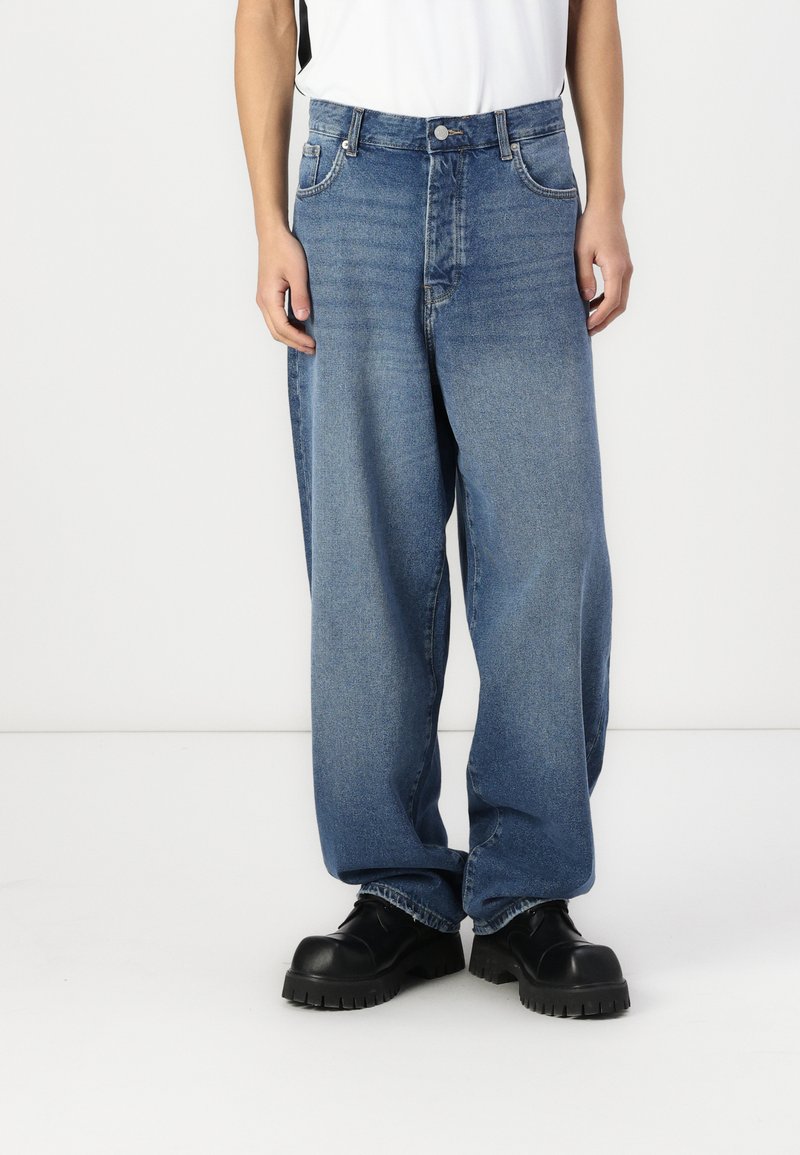 Light blue loose-fitting denim jeans with a high waist, five-pocket design, and visible stitching, paired with black chunky shoes.