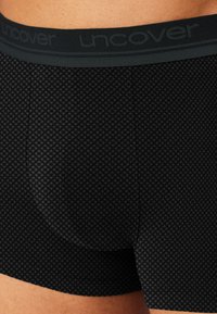 Schwarze Boxershorts aus weichem Stoff mit einem strukturierten Rautenmuster und einem breiten Bund mit "uncover"-Branding in dunkelgrau.