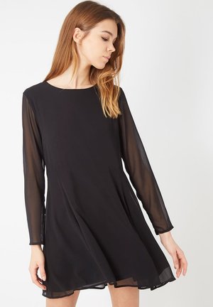 Vestido negro con mangas largas de tul, escote redondo y silueta acampanada. Tejido ligero con una textura suave y un diseño fluido.