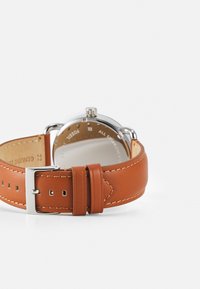Montre avec bracelet en cuir marron et boîtier en acier inoxydable argenté. Présente une finition polie et un design minimaliste et épuré.