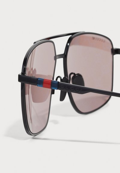 Okulary przeciwsłoneczne z czarną oprawką, różowymi przyciemnianymi szkłami i czerwono-niebieskim paskiem na zausznikach, z wytłoczonym logo Gucci.