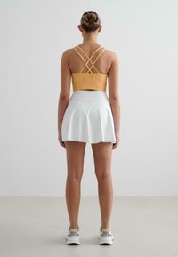 Heled oranž sportlik cropped top ristatud rihmadega, koos valge lühikese seeliku ja valgete tossudega, mis täiendavad kostüümi.