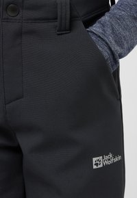 Svarta utomhusbyxor tillverkade av slät, hållbar tyg. Har en framficka, tryckknappsstängning och en logotyp i ljusgrått på benet.