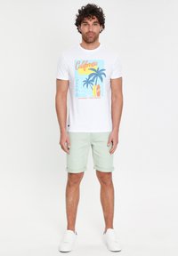 Miestenska biela tričko s potlačou Kalifornie, krátke rukávy, svetlozelené bavlnené šortky a biele tenisky. Pohodlný letný outfit.