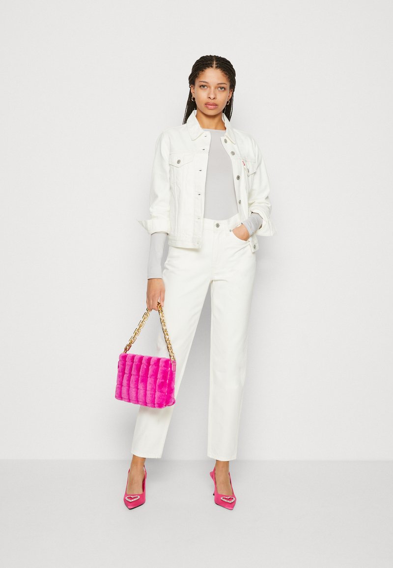 Giacca di denim bianca, top grigio chiaro, pantaloni bianchi, borsa trapuntata rosa con catena dorata e décolleté rosa a punta con dettagli a forma di cuore.