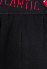 Czarny prążkowany materiał z czarnym pasem w talii, na którym znajduje się napis "ROMANTIC" w kolorze czerwonym oraz czerwony pikselowany symbol serca.