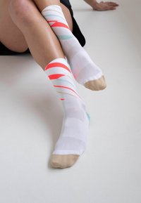 Weiße Socken mit mehrfarbigen Streifen in Rot, Türkis und Beige. Mit einer einfarbigen beigen Zehenpartie und atmungsaktivem Mesh-Textil.