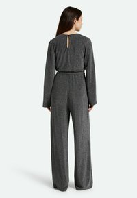 Mono gris con mangas largas, piernas amplias y tejido texturizado. Presenta un detalle en forma de llave en la espalda y una cintura ajustada.