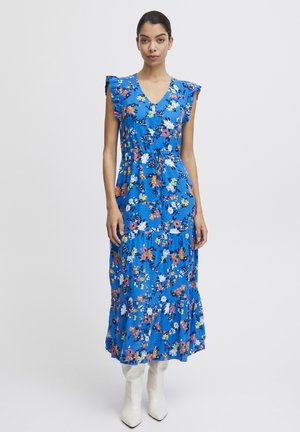 Vestido maxi floral azul con mangas acampanadas, escote en V, cintura ceñida y falda de volantes. Llevado con botas blancas hasta el tobillo.