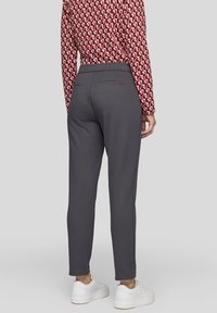 Grau gemusterte, schmal zulaufende Hosen mit glatter Textur, elastischem Bund, Rückentaschen und kombiniert mit weißen Sneakern.