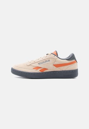 Zemslīpes bēšas un oranžas Reebok sporta kurpes ar pelēku zoli, sānu logo un šņorēm, attēlotas uz baltas virsmas, redzamas no ārpuses.