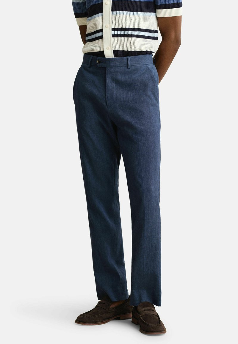 Uomo che indossa pantaloni eleganti blu navy, mocassini in pelle scamosciata marrone e una maglietta a maniche corte a righe orizzontali blu navy e crema.