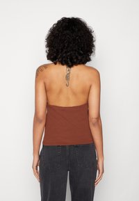 Top sem alças castanho canelado, ajustado ao corpo, textura suave, combinado com jeans pretos de cintura alta, exibindo tatuagens nas costas e nos ombros.