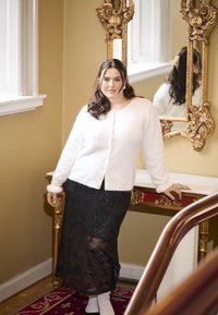 White fuzzy cardigan over a black sequined skirt featuring a geometric pattern. Accents include pearl details on the cardigan and ornate mirror.