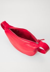 Red leather shoulder bag with a smooth texture, zip closure, and a side handle. The interior features a pocket and a branded label.