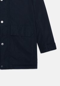 Navy blue jacket made of sturdy fabric, featuring a buttoned front, a patch pocket on the chest, and a folded cuff detail.