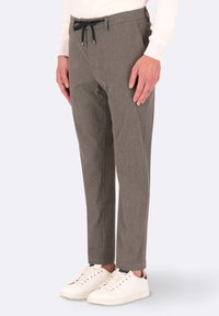 Pantaloni grigi su misura realizzati in tessuto testurizzato, con un laccio nero e tasche laterali. Indossati con sneaker bianche.