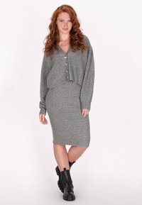 Graues Ripp-Strickset mit einem cropped Top mit Knopfdetails und einem knielangen Rock, kombiniert mit schwarzen Stiefeletten.