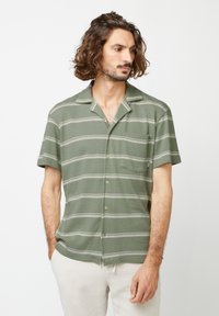 Chemise verte à manches courtes, avec des rayures blanches horizontales, col plat et poche poitrine. Tissu doux et texturé.