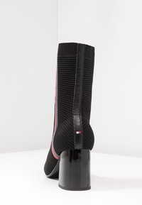 Botín negro hasta el tobillo con parte superior de textil acanalado, franja de acento rosa, tacón bloque negro brillante y detalle del logo en el lateral del tacón.