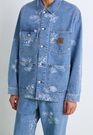 Denimjakke med hvide grafiske tryk, fire forlommer inklusive en med brun logo-patch, båret over matchende blå jeans med lignende tryk.