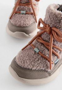 Lila Fleece-Ankleboot mit braunen Wildleder-Akzenten, ausgestattet mit geflochtenen Schnürsenkeln und einer strukturierten Gummisohle. Seitliche Anbringung für die Schnürsenkel.