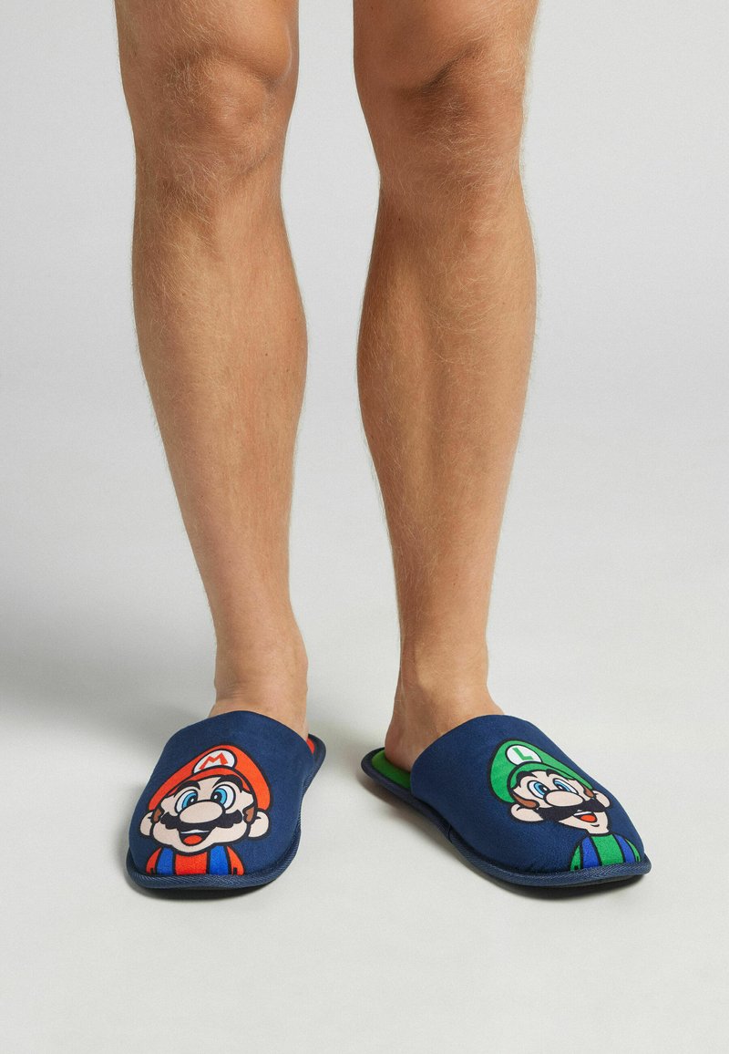 Blå tygtofflor med Mario- och Luigi-design, med en kontrasterande grön innersula och platta sulor.
