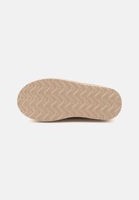 Semelle de chaussure en caoutchouc beige avec un motif ondulé, de forme arrondie et d'une texture lisse. Pas de marque visible ni de détails supplémentaires.